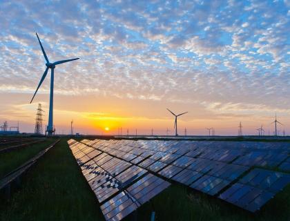 Renewable energy farm at sunset featuring solar panels in the foreground and wind turbines in the background, symbolizing sustainable power solutions and environmental innovation.